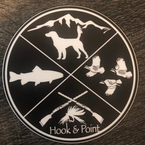May include: Black and white sticker with a mountain, dog, fish, birds, crossed rifles, a fly, and the text "Hook & Point".