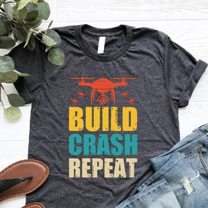 a t - shirt that says build crash repeat next to a pair of jeans and