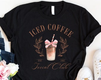 May include: Black t-shirt with a graphic of a glass of iced coffee with a pink bow and the text "ICED COFFEE EST. 1982 Social Club".