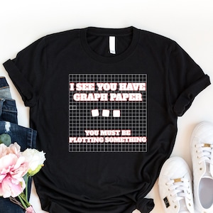 May include: Black t-shirt with a white graphic that says "I see you have graph paper. You must be plotting something." The graphic is on a grid pattern.