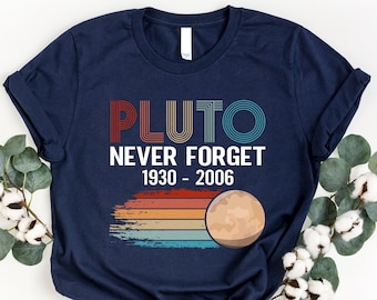 Op de afbeelding: Een marineblauw T-shirt met een retro-grafische afbeelding met de tekst "Pluto Never Forget 1930-2006" en een gestileerde afbeelding van Pluto.