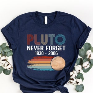 May include: A navy blue t-shirt with a retro-style graphic that says "Pluto Never Forget 1930-2006" and a stylized image of Pluto.