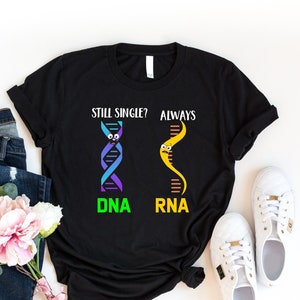May include: Black t-shirt with a graphic of two DNA strands, one labeled "DNA" and the other labeled "RNA". The DNA strand has a face and the text "Still Single?" above it. The RNA strand has a face and the text "Always" above it.