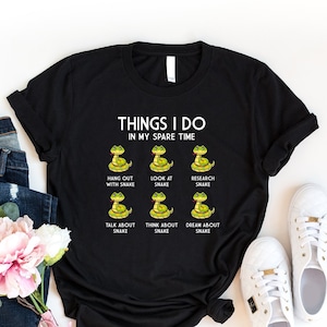 May include: Black t-shirt with a white graphic that says "Things I do in my spare time" and features a series of cartoon snakes with text below each snake that says "Hang out with snake", "Look at snake", "Research snake", "Talk about snake", "Think about snake", and "Dream about snake".