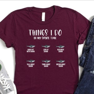 May include: A maroon t-shirt with the text "THINGS I DO IN MY SPARE TIME" and a grid of six images of sharks with text describing activities related to sharks.