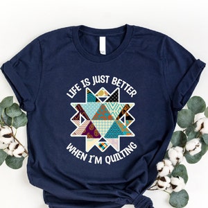 May include: Navy blue t-shirt with a white graphic that says "Life is just better when I'm quilting". The graphic features a colorful patchwork quilt design in the shape of a star.