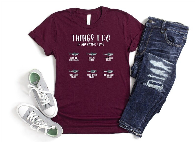 May include: A maroon t-shirt with the text "THINGS I DO IN MY SPARE TIME" and a grid of six images of sharks with text describing activities related to sharks.