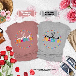 May include: Two short-sleeved crew neck t-shirts, one in heather mauve and one in athletic heather, each featuring a graphic of a computer icon and the text "Computer Lab TEACHER" surrounded by a circular border of colorful educational words.
