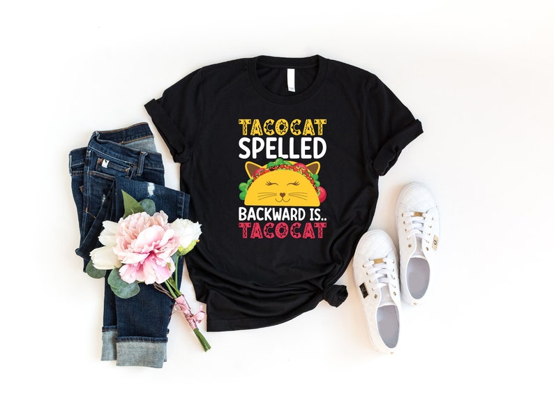 Pu&ograve; includere: Maglietta nera con una grafica bianca di un gatto che indossa un taco. Il testo sulla maglietta recita "Tacocat spelled backward is... Tacocat."
