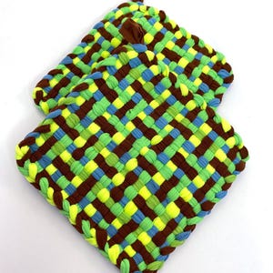 May include: Two woven pot holders in brown, green, yellow, and blue. The pot holders are made from woven fabric strips.
