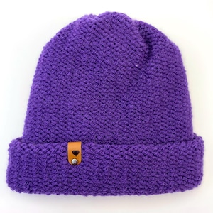 May include: Purple knitted beanie with a brown leather patch featuring a small heart.