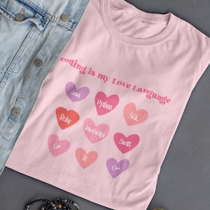 May include: Pink t-shirt with the text "coding is my Love Language" and hearts with different programming languages written inside: Java, Python, SOL, Ruby, JavaScript, Swift, C#, R, C++