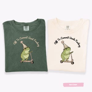 May include: Two t-shirts, one moss green and one ivory, each with a graphic of a frog on a scooter wearing a party hat. The text "Off To Commit Aunt Foolery" and "Off To Commit Uncle Foolery" are printed on the shirts.