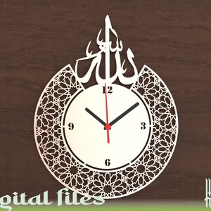 May include: White clock with Arabic calligraphy and a geometric pattern around the clock face. The clock face has black hands and red hour hand. The clock face has numbers 12, 3, 6, and 9.