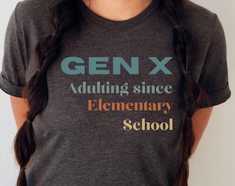 May include: A dark gray t-shirt with the text "GEN X Adulting since Elementary School" in colorful lettering.
