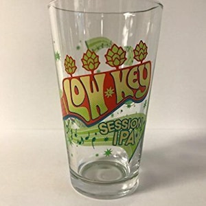May include: A clear glass pint glass with a colorful design featuring the words "Low Key Session IPA" and a graphic of musical notes and hops.