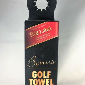 May include: Black box with "JOHNNIE WALKER Red Label" branding and a "Bonus GOLF TOWEL" label in gold. The top has a circular cutout for hanging. The box is black with red and gold accents.