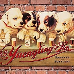 May include: A vintage metal sign featuring four puppies with bottles and glasses of beer. The sign reads "A.G. Yuengling & Son, Brewers and Bottlers" in red script against a tan background, set against a brick wall.