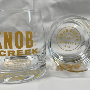 May include: Two clear glass tumblers with a gold Knob Creek logo. The logo says "Knob Creek" and "KY. US" on one tumbler and "Knob Creek Clermont KY Quality Std." on the other.