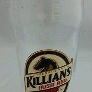 May include: A clear glass beer mug with a Killian's Irish Red label. The label features a horse head and the text "George Killian's Irish Red" in a gold and red color scheme.