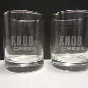 May include: Two clear glass tumblers with a silver rim. Each tumbler has the words "Knob Creek" etched on the front.