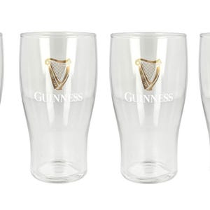 May include: Four clear pint glasses with the Guinness logo. Each glass has a gold harp emblem and the word "Guinness" printed in white. The glasses are empty and have a classic pint glass shape.