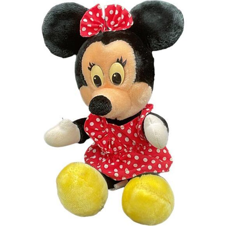 May include: A plush Minnie Mouse doll with black ears, a red polka-dot bow, and a red polka-dot dress. The doll has a tan face, black nose, and yellow feet. The doll is a classic children's toy.