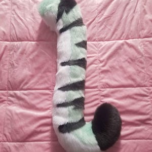 Può includere: Una lunga coda soffice, a strisce verdi e bianche con una punta nera. La coda è realizzata in pelliccia sintetica ed è progettata per assomigliare alla coda di un gatto.