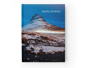 May include: A hardcover travel journal with a scenic landscape cover. The cover features a snow-covered mountain under a dark blue sky, with the words "TRAVEL JOURNAL" printed at the top.
