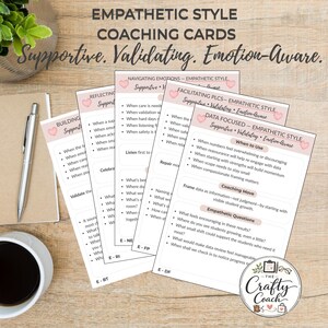 May include: A set of Empathetic Style Coaching Cards, white with pink accents, with the words 'Supportive, Validating, Emotion-Aware'. The cards contain coaching prompts and questions. A pen and a cup of coffee are also visible on a wooden surface.