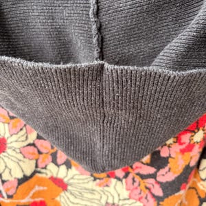 May include: Close-up of a dark gray hooded sweatshirt with a floral pattern. The hood is a solid dark gray, while the interior and lower portion of the sweatshirt feature a pattern of large flowers in cream, orange, and pink.