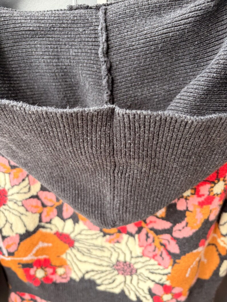 May include: Close-up of a dark gray hooded sweatshirt with a floral pattern. The hood is a solid dark gray, while the interior and lower portion of the sweatshirt feature a pattern of large flowers in cream, orange, and pink.