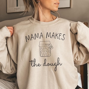 May include: A beige sweatshirt with the text "Mama Makes the Dough" and a drawing of a jar with a tag that says "Good Stuff" on it.