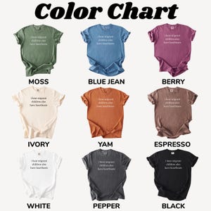 Pu&ograve; includere: Una tabella colori mostra nove magliette in vari colori: muschio, blu jeans, bacca, avorio, igname, espresso, bianco, pepe e nero. Ogni maglietta ha il testo "I hear migrant children also have heartbeats."