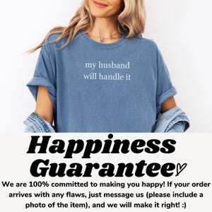 May include: A blue t-shirt with the text "my husband will handle it" in white. The shirt is part of a clothing collection. The bottom of the image has the text "Happiness Guarantee" and a customer satisfaction statement.