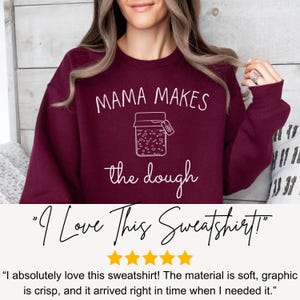 May include: Burgundy sweatshirt with white text that reads "Mama Makes the Dough" and a graphic of a jar with a label that says "Dough".
