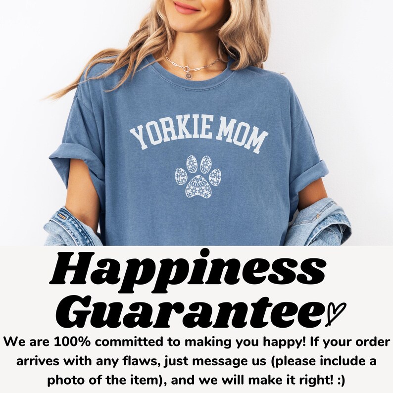 May include: A blue t-shirt with the text "YORKIE MOM" in white, above a white paw print design. The shirt is part of a clothing collection. The image also includes the text "Happiness Guarantee".