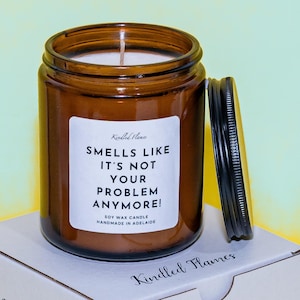 May include: A brown glass jar candle with a black lid. The label on the candle reads "Smells Like It's Not Your Problem Anymore!" The candle is made from soy wax and handmade in Adelaide.