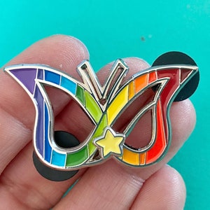May include: A rainbow-colored butterfly pin with a yellow star in the center. The pin is made of metal and has a silver finish.