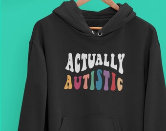 Może przedstawiać: Czarna bluza z kapturem z napisem "Actually Autistic" w tęczowych literach.