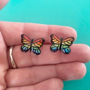 Peut inclure: Une paire de boucles d'oreilles en forme de papillon arc-en-ciel. Les papillons sont noirs avec des ailes arc-en-ciel.