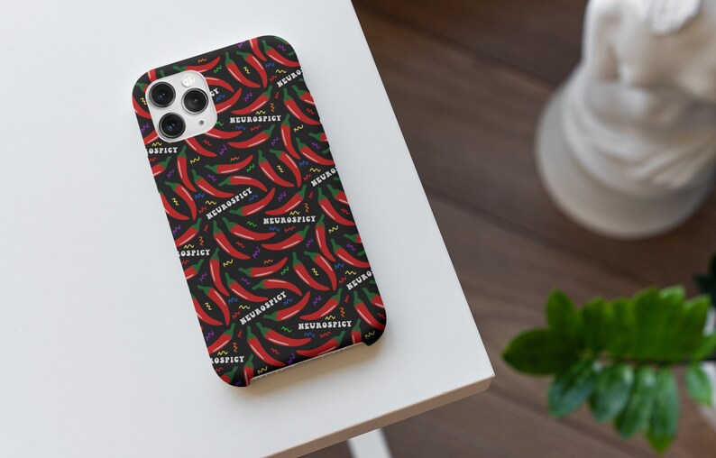 Puede incluir: Una funda de tel&eacute;fono negra con un chile rojo y el texto "Neurospicy" repetido en un patr&oacute;n.