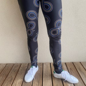 Puede incluir: Leggings negros con un patr&oacute;n de s&iacute;mbolo de infinito colorido. Los leggings los lleva una persona con zapatillas blancas.