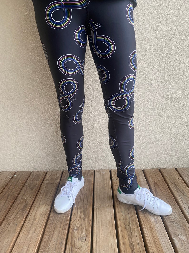 Puede incluir: Leggings negros con un patr&oacute;n de s&iacute;mbolo de infinito colorido. Los leggings los lleva una persona con zapatillas blancas.