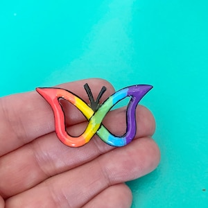 May include: A rainbow-colored butterfly charm with black outlines. The butterfly is made of resin and has a glossy finish.