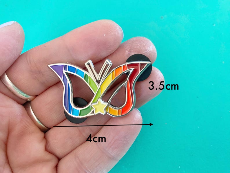 May include: Rainbow enamel pin shaped like a butterfly with a star in the center. The pin is 4 inches wide and 3.5 inches tall.