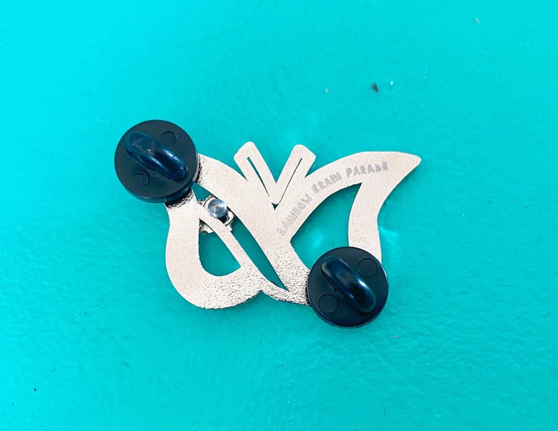 May include: Silver butterfly pin with black rubber backings. The pin features the text "Rainbow Brain Parade" on the back.