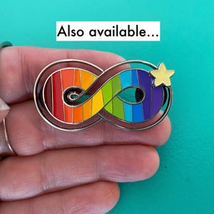 May include: A rainbow infinity symbol with a yellow star on a silver background. The infinity symbol is made of enamel and has a rainbow color scheme. The star is also made of enamel and is yellow. The background is silver.