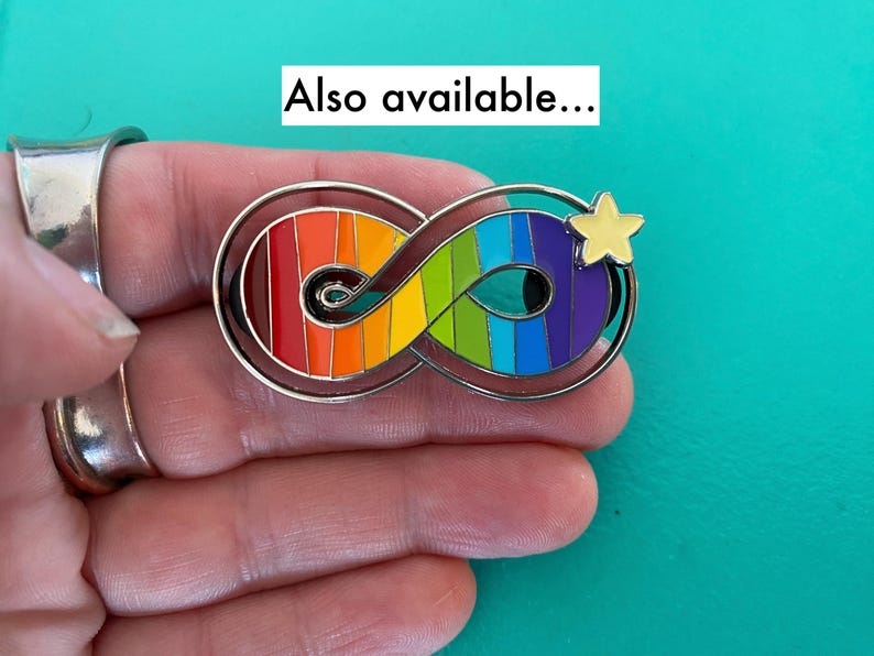 May include: A rainbow infinity symbol with a yellow star on a silver background. The infinity symbol is made of enamel and has a rainbow color scheme. The star is also made of enamel and is yellow. The background is silver.