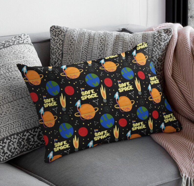 Puede incluir: Una almohada negra y blanca con un patr&oacute;n repetido de planetas, estrellas y el texto "SAFE SPACE".